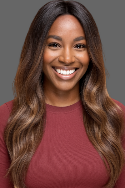 Confident Black woman with medium brown skin wearing Sienna Wavy Wig, off-black with ombre caramel highlights, light beige background
